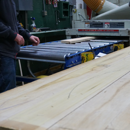 A Highland Hardwoods woodworker planes a piece of lumber in a wood planer.